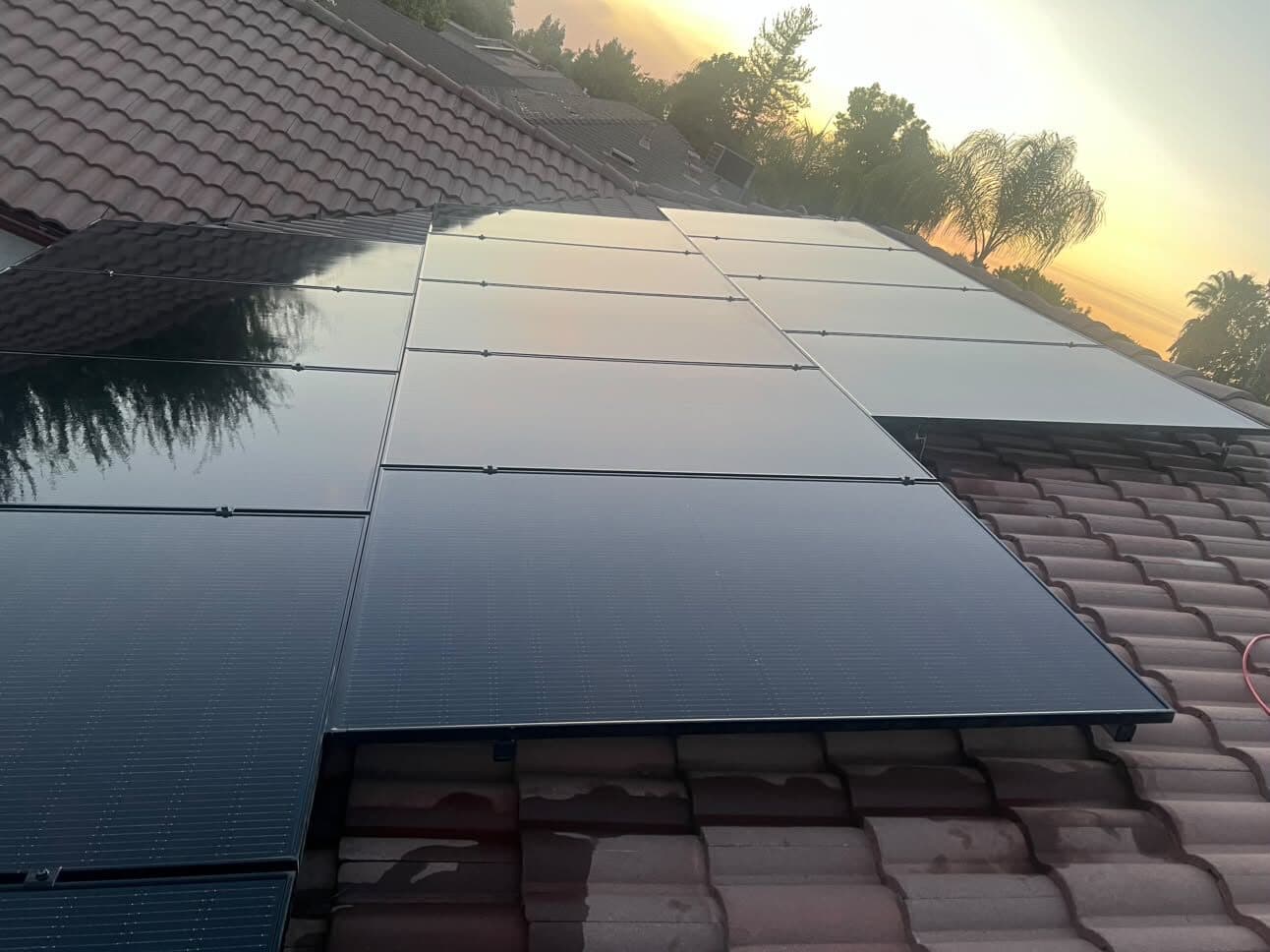 Freshly cleaned solar panels on a tile roof under a golden-hour sky
