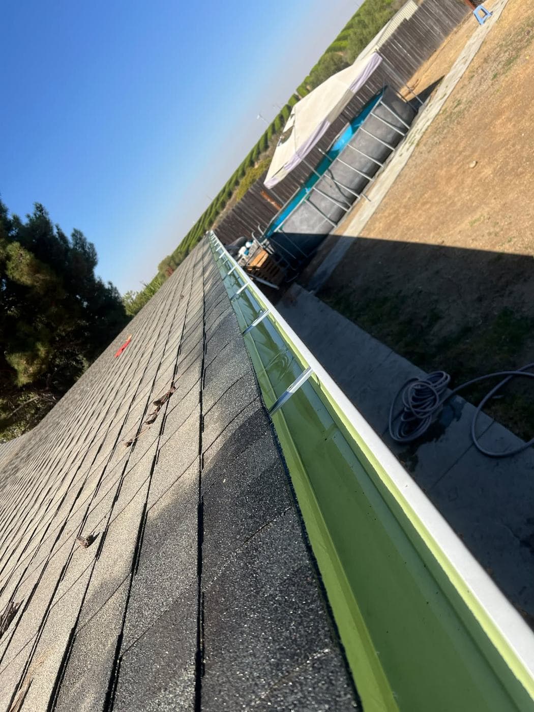 Clear gutter run along a roofline after service, with the backyard visible below