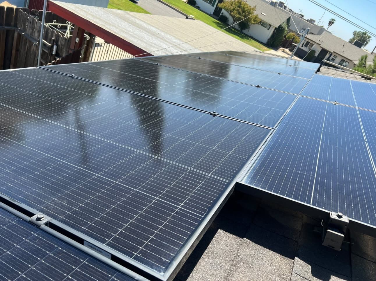 Freshly cleaned solar panels on a shingle roof — wide view across a Madera neighborhood