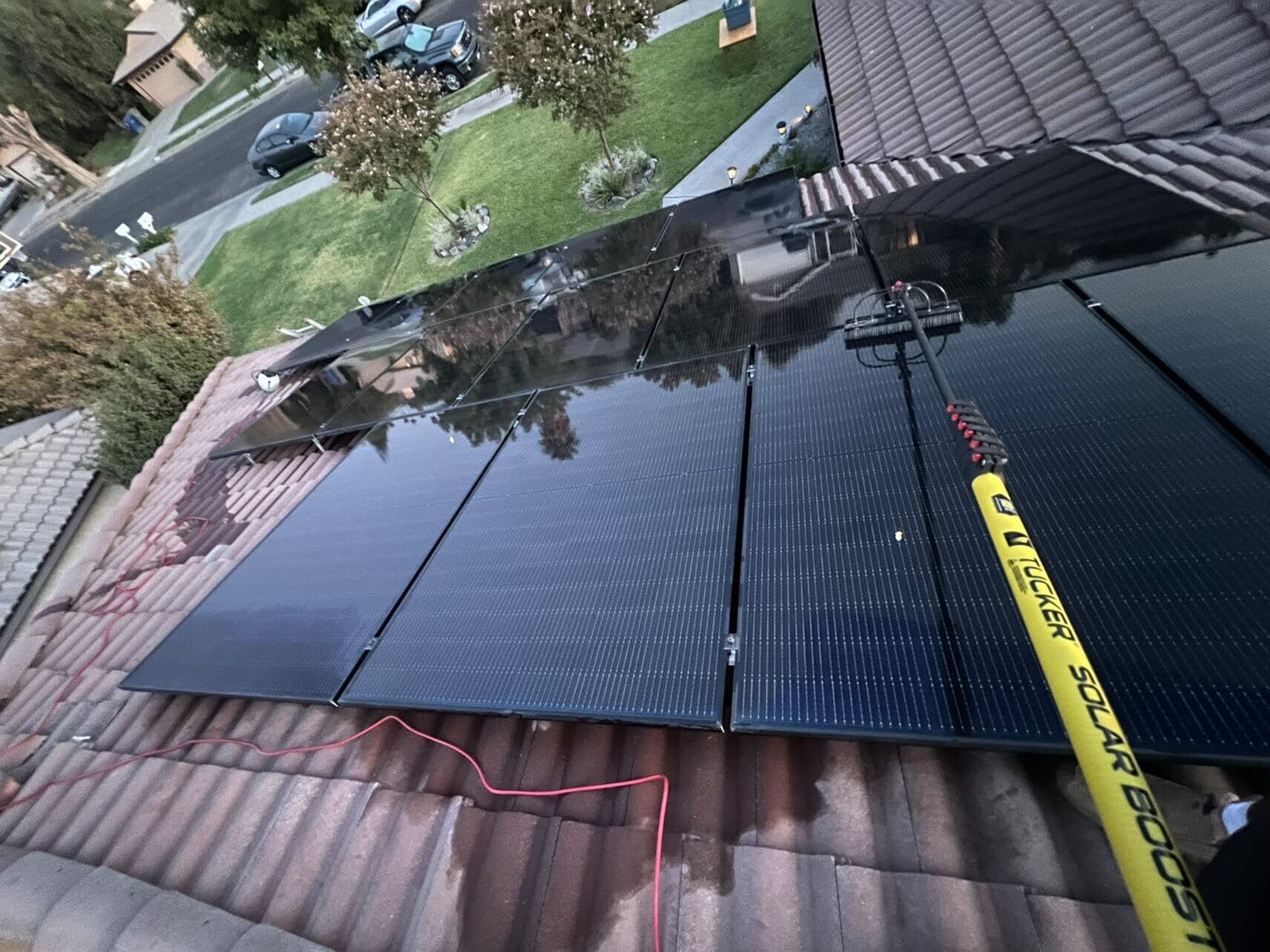 Water-fed extension pole and brush washing solar panels mid-clean on a tile roof